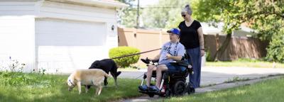 Mother waking alongside her son in a wheelchair walking their two dogs