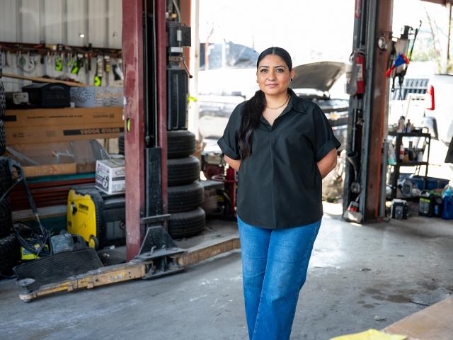 Woman standing wtih her hands behind her back in a mechanics garage