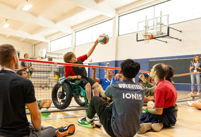 Teen in wheelchair spikes volleyball over the net in adaptive volleyball game