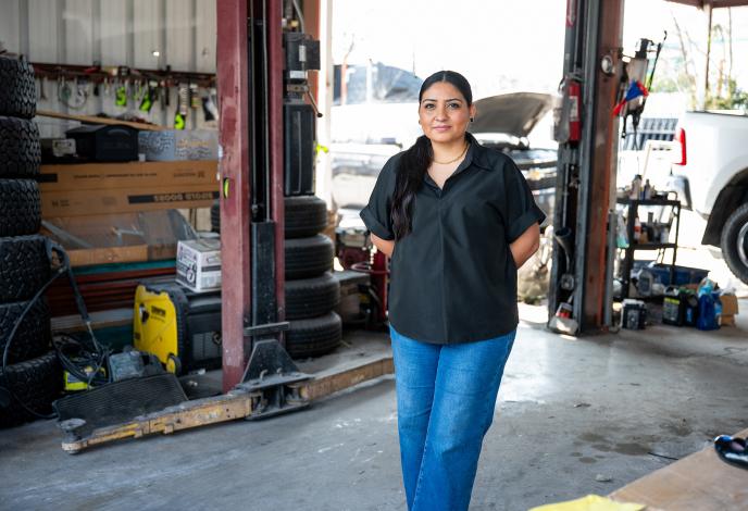 Woman standing wtih her hands behind her back in a mechanics garage