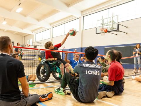 Teen in wheelchair spikes volleyball over the net in adaptive volleyball game