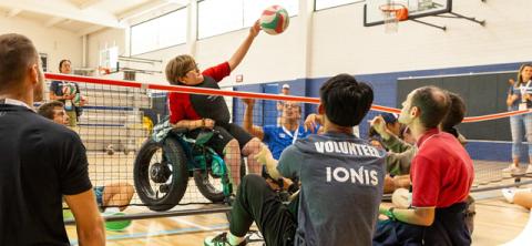 Teen in wheelchair spikes volleyball over the net in adaptive volleyball game