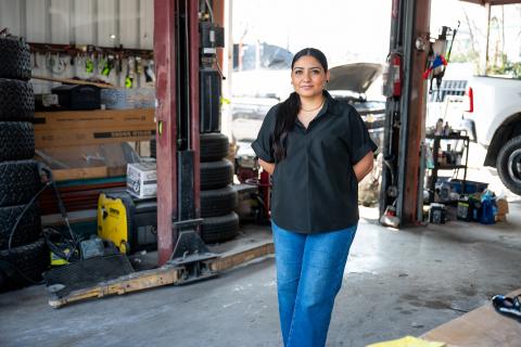Woman standing wtih her hands behind her back in a mechanics garage